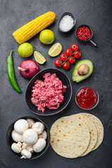 Wall Mural - Traditional mexican tortilla with a mix of ingredients, corn, meat, vegetables, salsa, sauce over black textured background, top view.