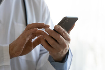 Crop close up of male doctor in white medical uniform hold modern smartphone gadget consult patient online, man GP physician use cellphone device, text message to client, medicine technology concept