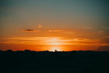 Wall Mural - Orange sunset with silhouettes of trees in the evening. Clouds over the contours of forest