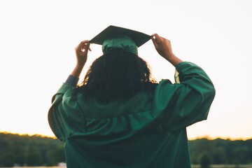 Young woman in a green academic dress holding a gown cap - the concept of graduation