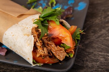 Wall Mural - Closeup shot of a juicy tortilla wrap with pulled meat, tomatoes, and greens