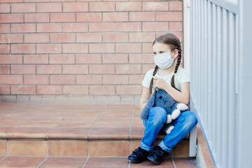 a girl in a mask with two pigtails sits on the street porch of the entrance and looks away