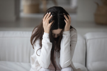 Close up hopeless unhappy young woman holding head, feeling depressed, lonely and misunderstood, sitting on couch alone, frustrated upset girl suffering from break up with boyfriend or divorce