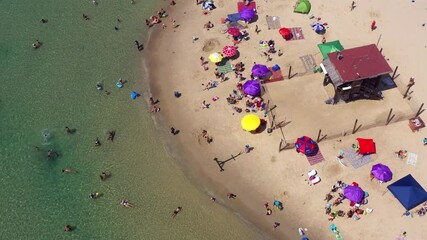 Wall Mural - Crowded public beach with colourful umbrellas and people in the water and relaxing on the sand, Aerial view.