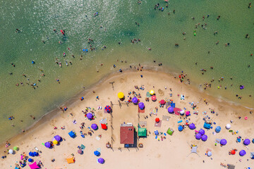 Wall Mural - Crowded public beach with colourful umbrellas and people in the water and relaxing on the sand, Aerial view.