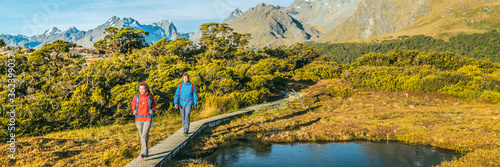 New Zealand Hiking. Panoramic banner of Young hiking couple walking on trail at Routeburn Track during. Hikers carrying backpacks tramping Key Summit Track, Fiordland National Park, New Zealand.