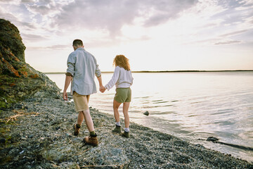 Canvas Print - Young amorous hikers in casualwear holding by hands while moving along coastline