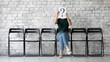 © fizkes - On grey brick wall background anonymous young woman sit on chair hiding her face behind paper with interrogation symbol. Doubtful female holding question mark sheet, problems and solutions HR concept
