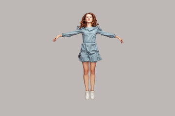 full length happy calm pretty girl in vintage ruffle dress levitating hovering in mid-air with raise