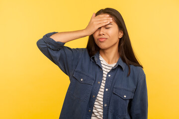 My fault! Portrait of sorrowful upset girl in denim shirt doing facepalm gesture, blaming herself for forgotten event, stupid mistake, bad memory. indoor studio shot isolated on yellow background