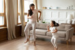 Energetic young vietnamese ethnic mother enjoying playtime with funny crazy asian child daughter, dancing to favorite disco music barefoot in modern living room, hobby weekend pastime indoors.