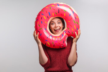 Optimistic funny girl looking through rubber ring with happy amazed expression, shouting for joy in anticipation of summer vacation, rest at seaside, travel concept. indoor studio shot isolated