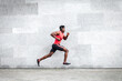 © Богдан Маліцький - African American guy runner runs fast forward against the background of the city wall, sports man train on the street