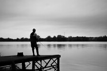 Silhouette Of A Fisherman Standing On The Pier, Black And White Photo