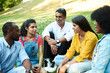© etonastenka - Afghan, black, mexican and indian chatting while sitting in the park on the grass. The concept of communication of different nationalities. Diverse people and friends