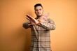 © Krakenimages.com - Young handsome man wearing casual shirt standing over isolated yellow background Rejection expression crossing arms doing negative sign, angry face