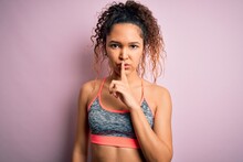 Beautiful Sportswoman With Curly Hair Doing Sport Wearing Sportswear Over Pink Background Asking To Be Quiet With Finger On Lips. Silence And Secret Concept.