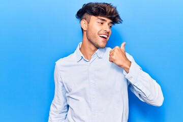 Wall Mural - Young hispanic man wearing casual clothes pointing thumb up to the side smiling happy with open mouth