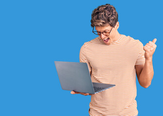 Young handsome man wearing glasses holding laptop screaming proud, celebrating victory and success very excited with raised arms