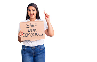 Poster - Young beautiful woman holding save our democracy cardboard banner surprised with an idea or question pointing finger with happy face, number one