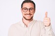 © Krakenimages.com - Young handsome man wearing casual clothes and glasses smiling happy and positive, thumb up doing excellent and approval sign