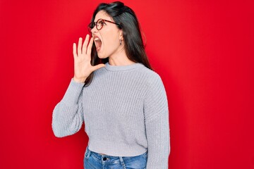 Canvas Print - Young beautiful brunette woman wearing casual sweater over red background shouting and screaming loud to side with hand on mouth. Communication concept.