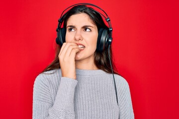 Canvas Print - Young beautiful girl wearing modern headphones listening to music over red background looking stressed and nervous with hands on mouth biting nails. Anxiety problem.