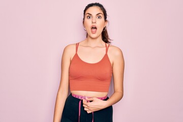 Poster - Young beautiful fitness woman wearing sport excersie clothes using measuring tape scared in shock with a surprise face, afraid and excited with fear expression