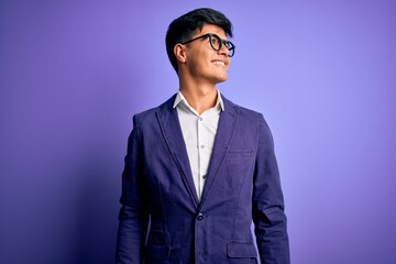 Poster - Young handsome business man wearing jacket and glasses over isolated purple background looking away to side with smile on face, natural expression. Laughing confident.