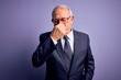 © Krakenimages.com - Grey haired senior business man wearing glasses and elegant suit and tie over purple background smelling something stinky and disgusting, intolerable smell, holding breath with fingers on nose.