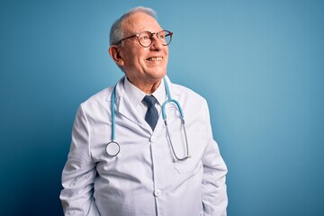 Sticker - Senior grey haired doctor man wearing stethoscope and medical coat over blue background looking away to side with smile on face, natural expression. Laughing confident.