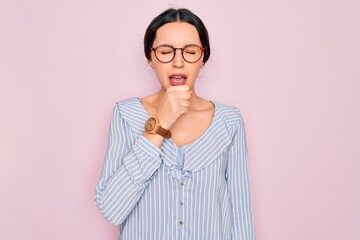 Wall Mural - Young beautiful woman wearing casual striped shirt and glasses over pink background feeling unwell and coughing as symptom for cold or bronchitis. Health care concept.