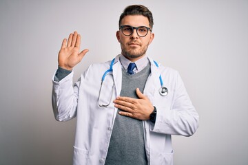 Wall Mural - Young doctor man with blue eyes wearing medical coat and stethoscope over isolated background Swearing with hand on chest and open palm, making a loyalty promise oath