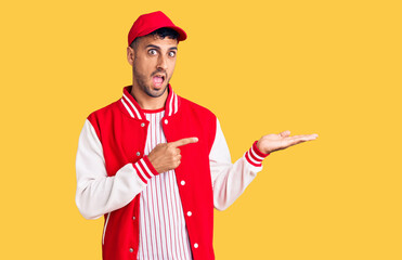 Canvas Print - Young hispanic man wearing baseball uniform amazed and smiling to the camera while presenting with hand and pointing with finger.