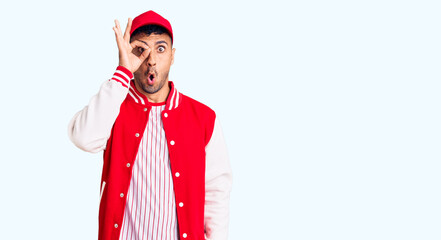 Canvas Print - Young hispanic man wearing baseball uniform doing ok gesture shocked with surprised face, eye looking through fingers. unbelieving expression.