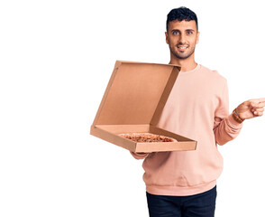 Poster - Young hispanic man holding delivery pizza box smiling happy pointing with hand and finger to the side