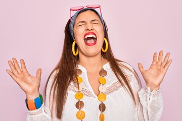 Canvas Print - Young hispanic hippie woman wearing fashion boho style and sunglasses over pink background celebrating mad and crazy for success with arms raised and closed eyes screaming excited. Winner concept