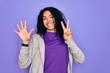 © Krakenimages.com - Young african american sporty woman wearing casual sweatshirt over purple background showing and pointing up with fingers number seven while smiling confident and happy.