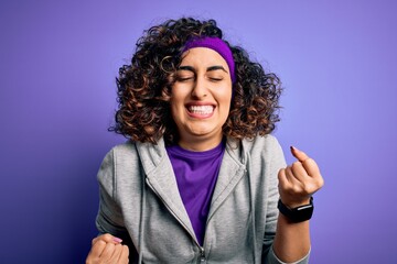 Sticker - Beautiful curly arab sportswoman doing sport wearing sportswear over purple background very happy and excited doing winner gesture with arms raised, smiling and screaming for success. Celebration.