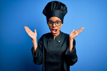 Wall Mural - Young african american chef woman wearing cooker uniform and hat over blue background celebrating crazy and amazed for success with arms raised and open eyes screaming excited. Winner concept