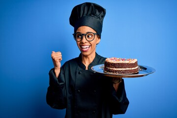 Wall Mural - Young african american baker woman wearing cooker uniform and hat holding cake pointing and showing with thumb up to the side with happy face smiling