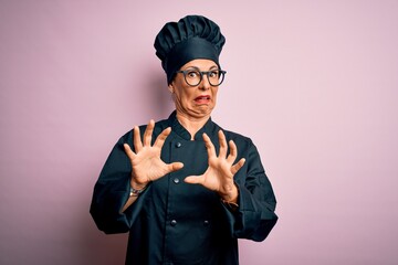 Poster - Middle age brunette chef woman wearing cooker uniform and hat over isolated pink background afraid and terrified with fear expression stop gesture with hands, shouting in shock. Panic concept.