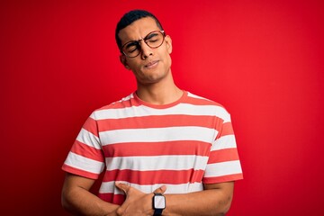 Young handsome african american man wearing casual striped t-shirt and glasses with hand on stomach because indigestion, painful illness feeling unwell. Ache concept.