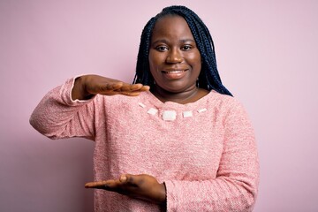 Sticker - African american plus size woman with braids wearing casual sweater over pink background gesturing with hands showing big and large size sign, measure symbol. Smiling looking at the camera. Measuring.