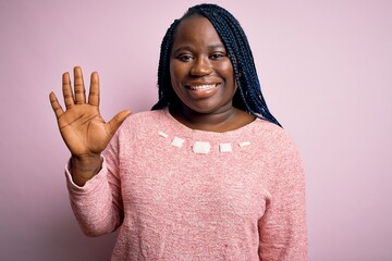 Poster - African american plus size woman with braids wearing casual sweater over pink background showing and pointing up with fingers number five while smiling confident and happy.