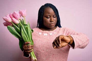 Wall Mural - Young african american plus size woman with braids holding bouquet of pink tulips flower Checking the time on wrist watch, relaxed and confident