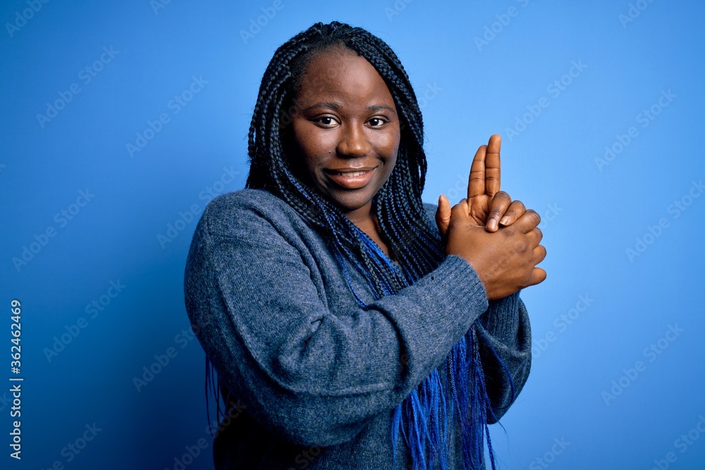 African american plus size woman with braids wearing casual sweater over blue background Holding symbolic gun with hand gesture, playing killing shooting weapons, angry face