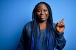 © Krakenimages.com - African american plus size woman with braids wearing casual sweater over blue background with a big smile on face, pointing with hand finger to the side looking at the camera.