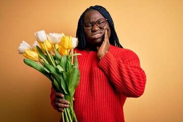 Sticker - Young african american plus size woman with braids holding bouquet of yellow tulips flower touching mouth with hand with painful expression because of toothache or dental illness on teeth. Dentist.