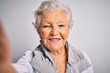 Senior beautiful grey-haired woman making selfie by camera over isolated white background with a happy face standing and smiling with a confident smile showing teeth